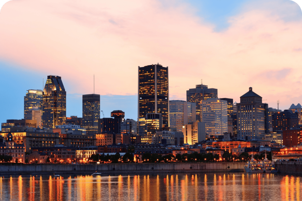 Montreal skyline at sunset with city lights reflecting on the water.