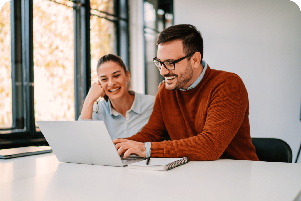 Two colleagues smiling while working together on a laptop in a bright office.